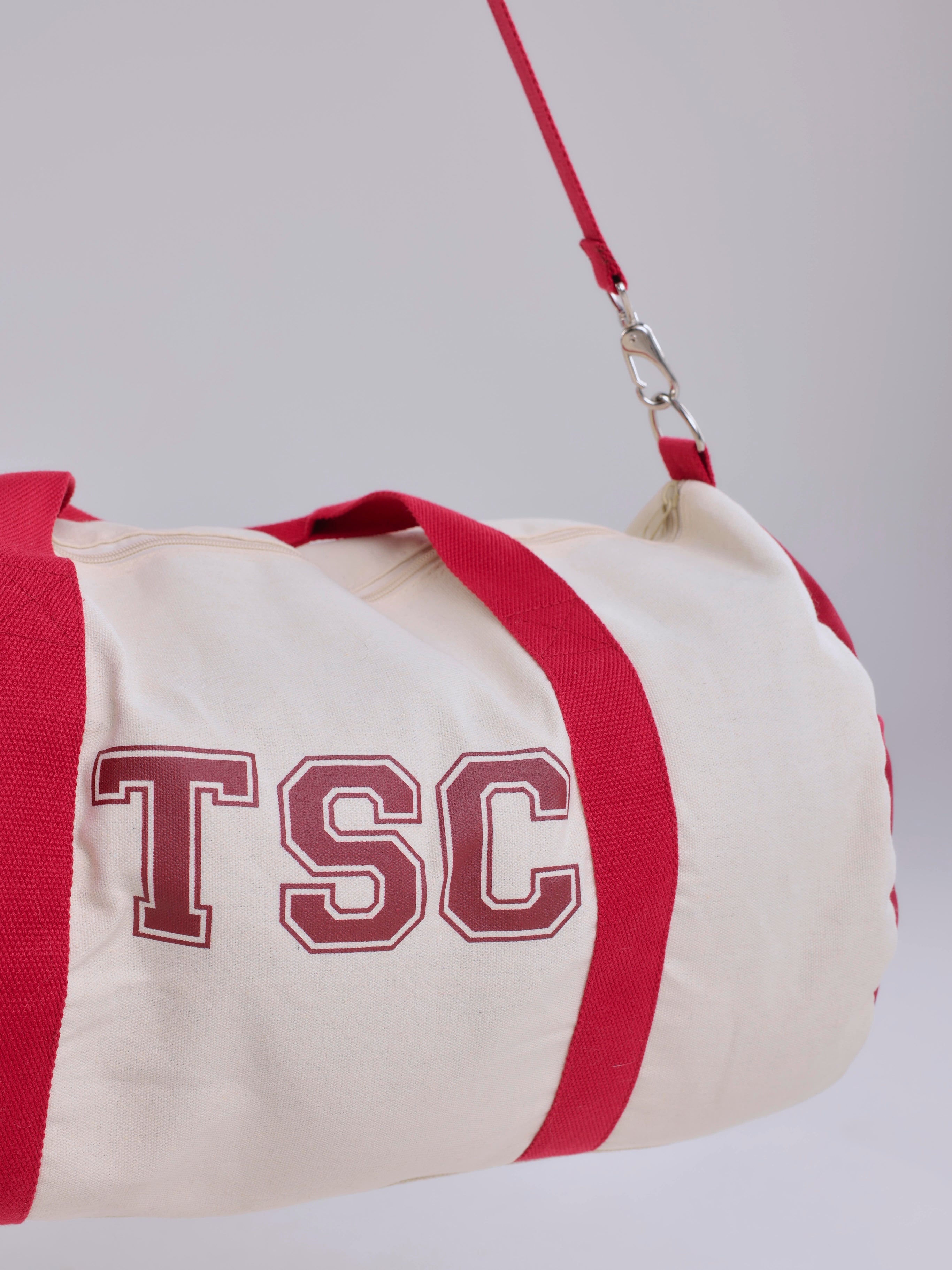 Canvas duffel bag with red accents and 'TSC' branding on a light gray background