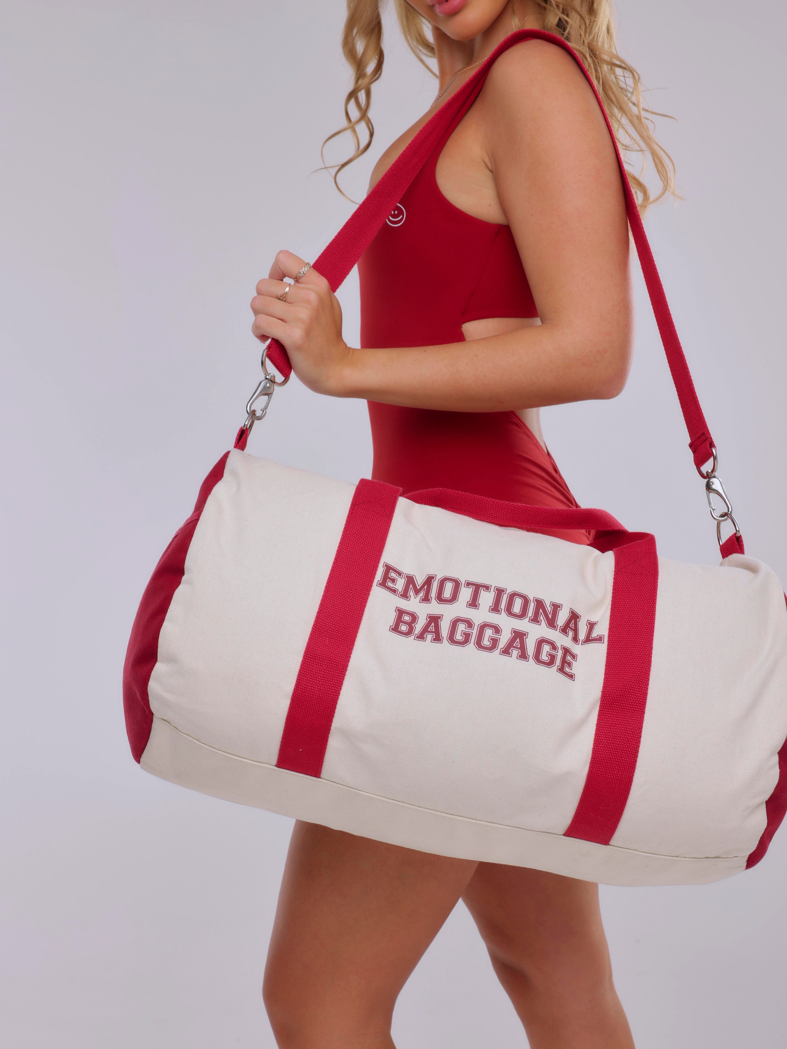 Person holding a duffel bag with 'EMOTIONAL BAGGAGE' text against a white background